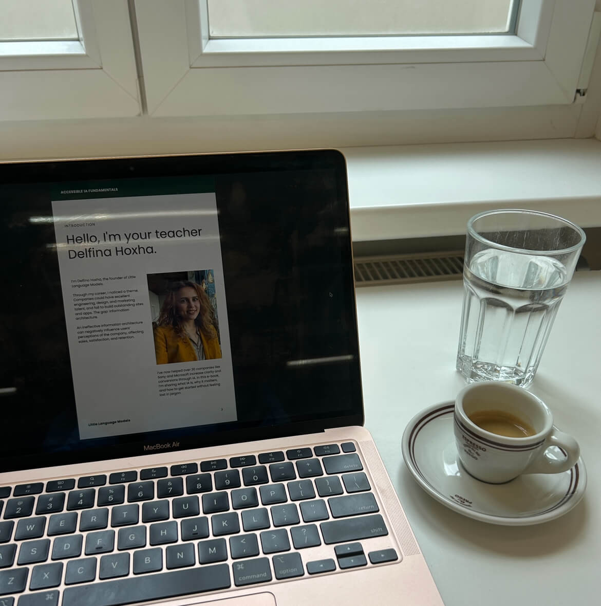 my laptop showing the introduction screen of my new ebook, an espresso cup, and a glass of water in front of my office window